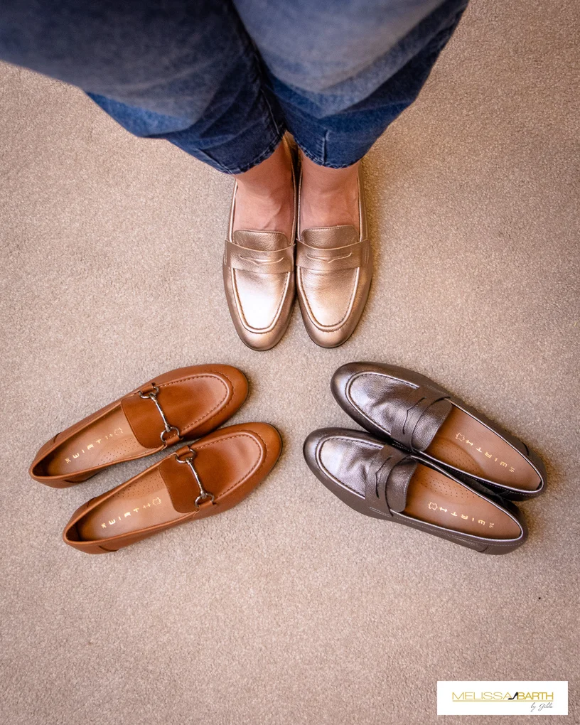 Foto superior mostrato 3 sapatos mocassim o da prte de cima é dourado e estão nos pés da modelo. O da lateral direira é cor de chumbo metalizado, o da esqueda é de couro marrom acastanhado. 