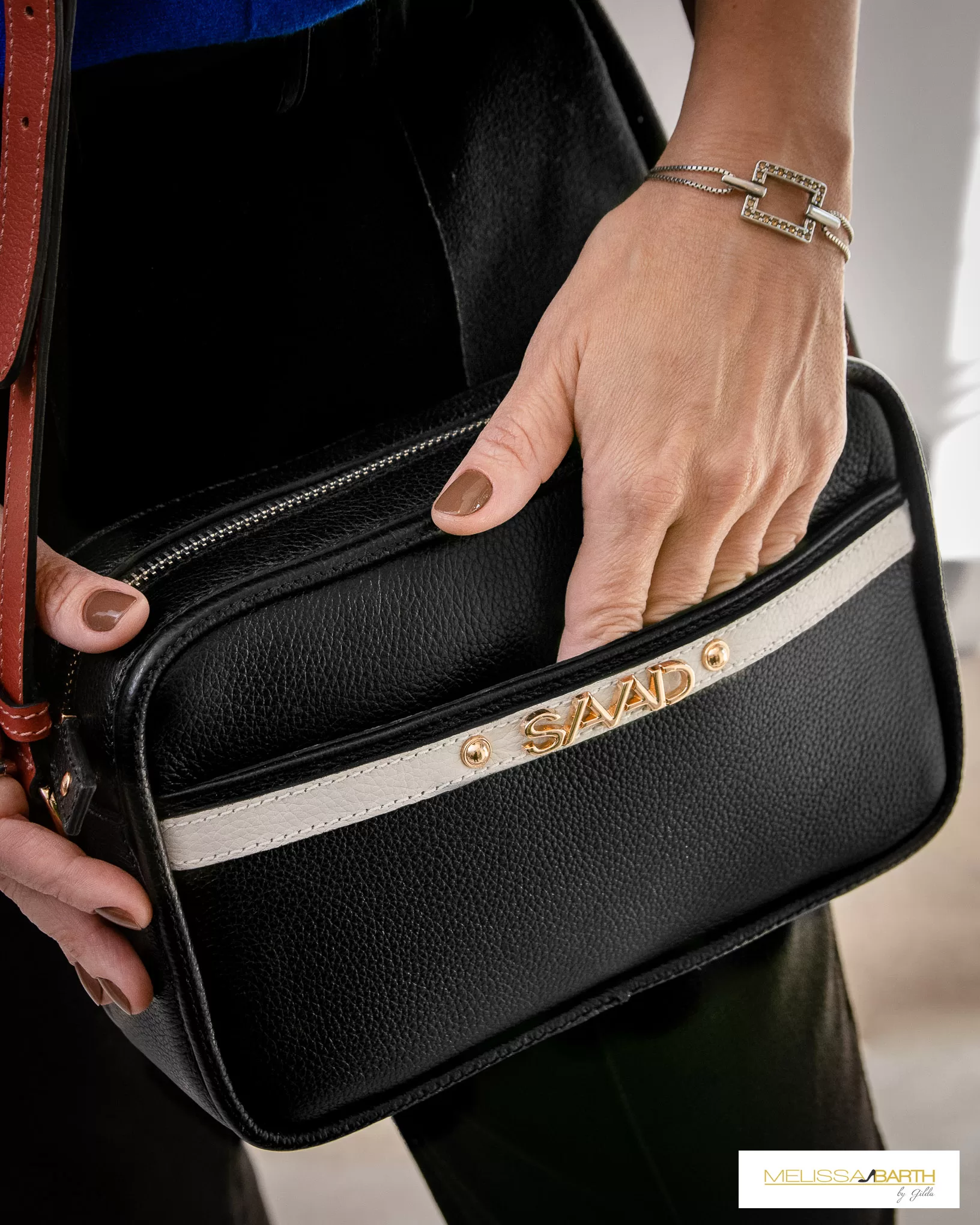 Modelo usando uma bolsa preta atemporal da marca saad vendida pela loja melissa barth by gilda em itapetininga, a foto mostra a parte externa da bolsa e a modelo esta com a mão parcialmente dentro de um dos compartimentos.